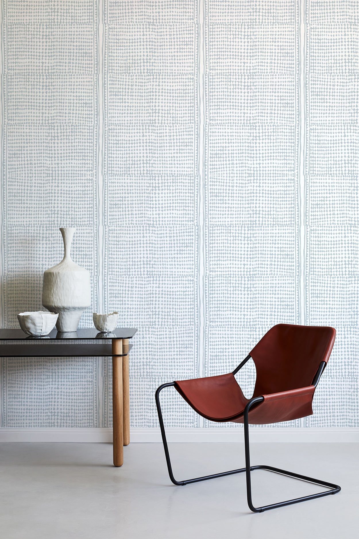 Modern interior with a brown chair, small table, and decorative items against a blue geometric wallpaper