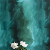 A vase of flowers stands in front of a wall papered in an abstract curvilinear pattern in mottled turquoise and black.