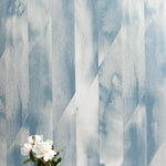 A vase of flowers stands in front of a wall papered in a linear geometric print in shades of blue and gray.