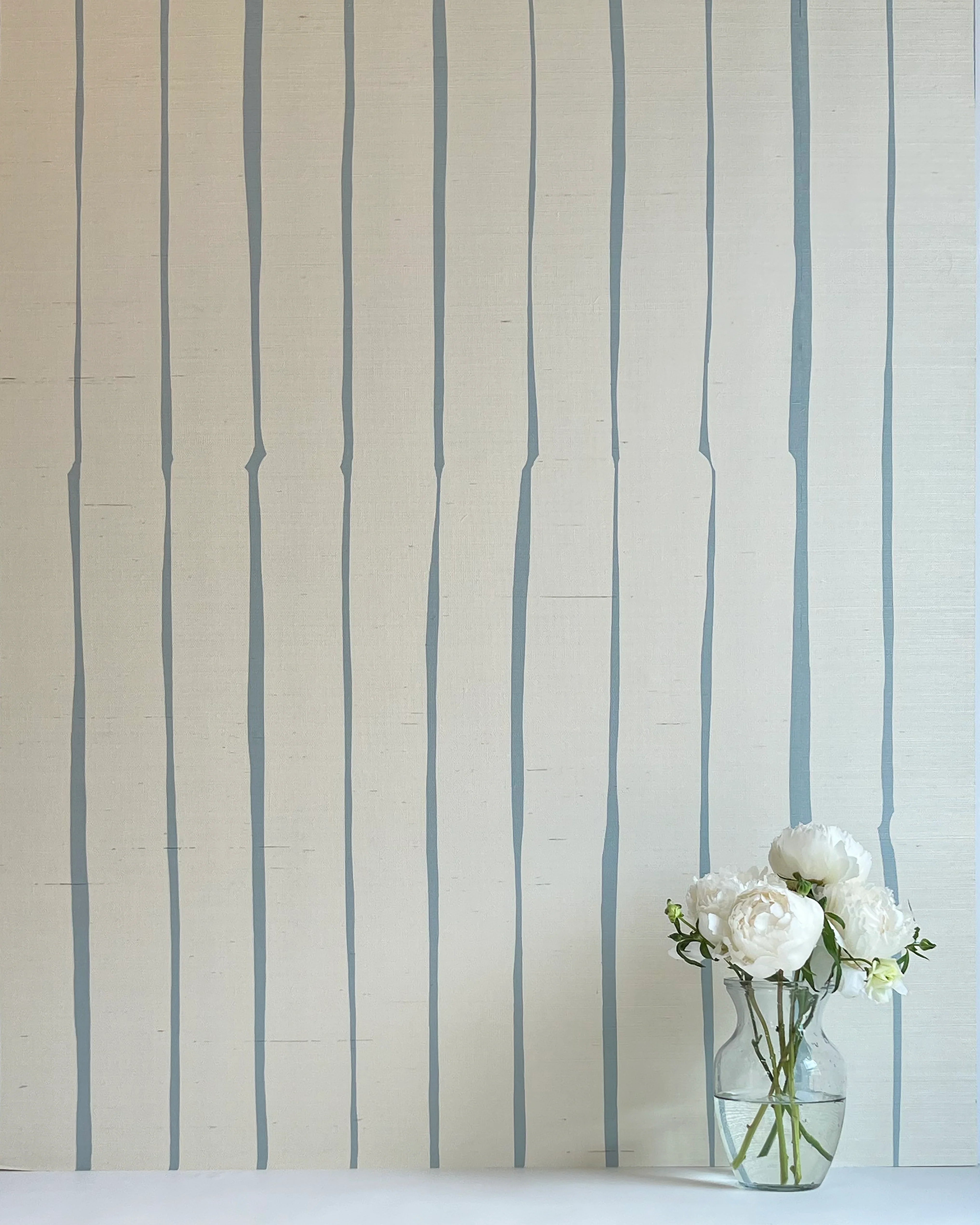 A vase of flowers stands in front of a wall covered in a playful irregular stripe print in blue on a cream field.