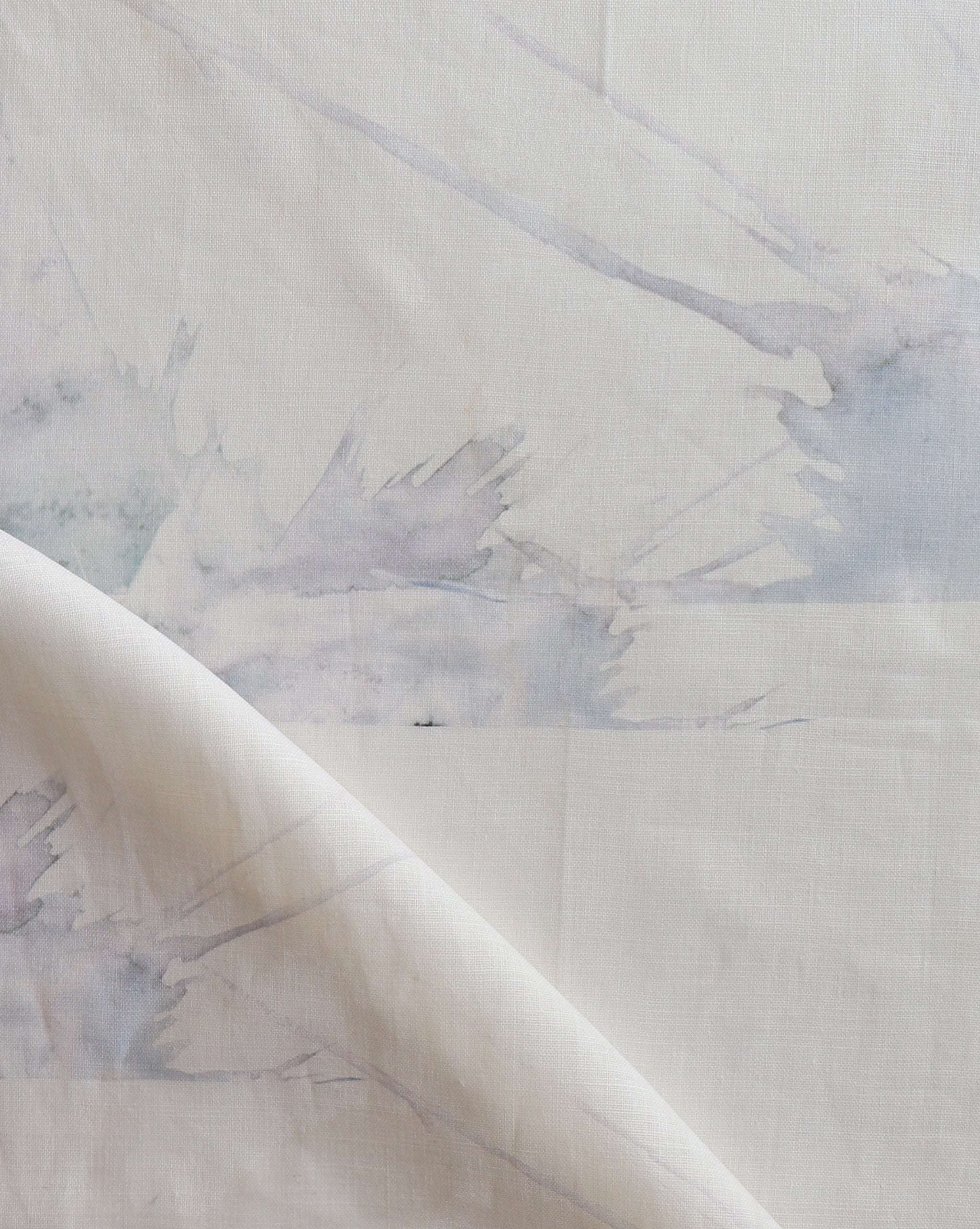 Draped fabric yardage in a watercolor splatter print in pastel purple and gray on a cream field.