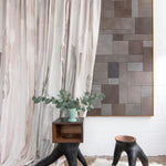 Modernist end tables stand in front of a curtain in a watercolor paint print in shades of pink, brown and gray on a cream field.