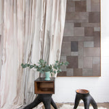 Modernist end tables stand in front of a curtain in a watercolor paint print in shades of pink, brown and gray on a cream field.