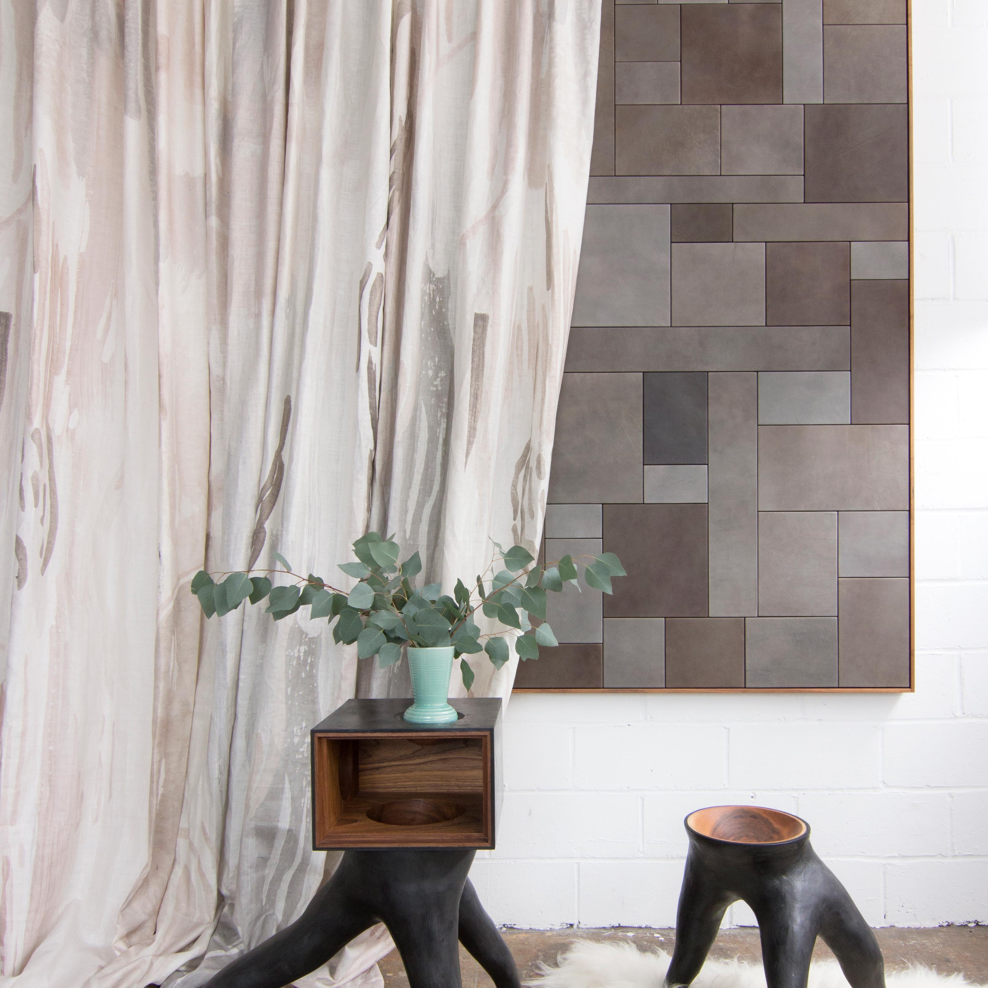 Modernist end tables stand in front of a curtain in a watercolor paint print in shades of pink, brown and gray on a cream field.