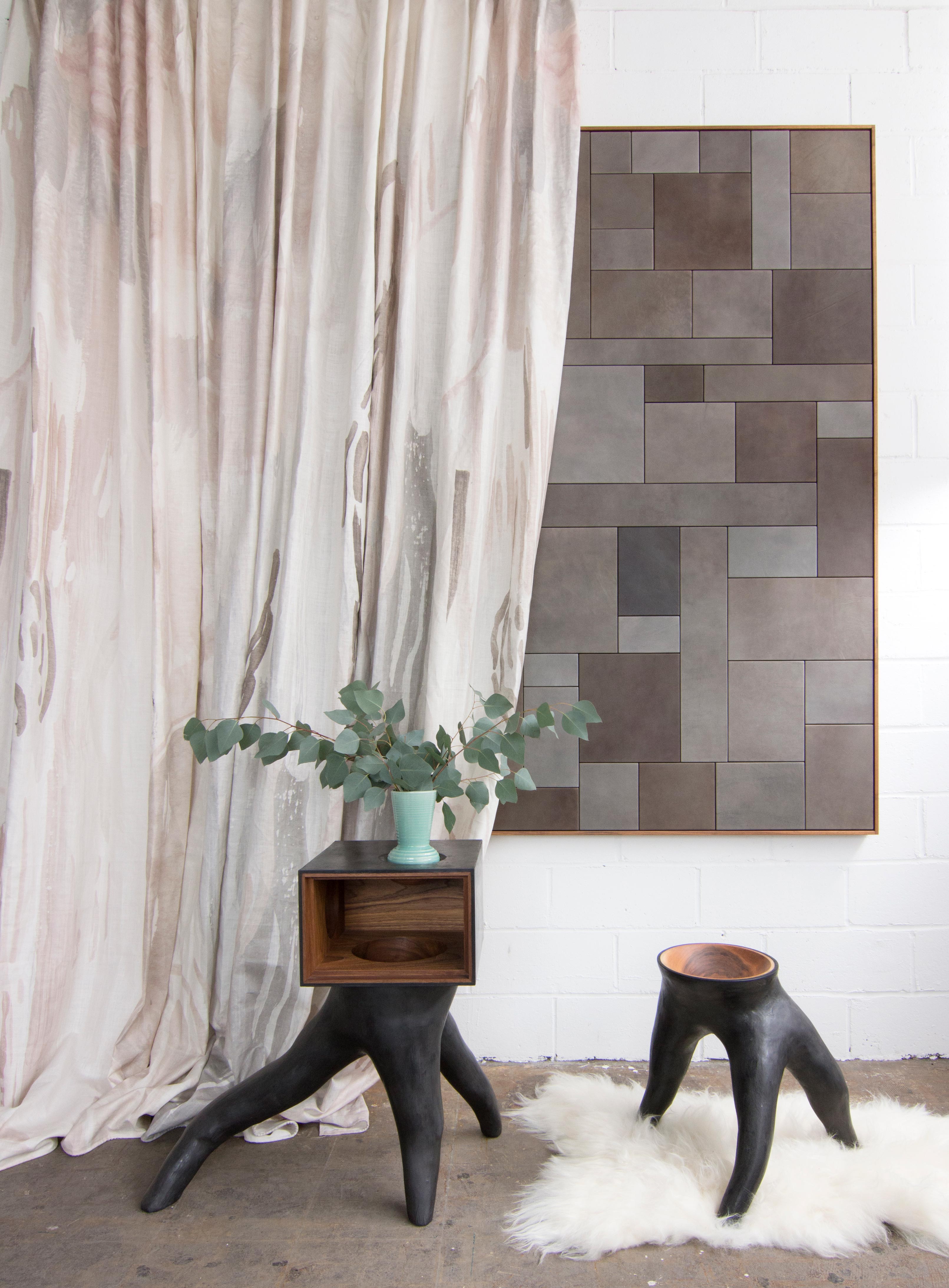 Modernist end tables stand in front of a curtain in a watercolor paint print in shades of pink, brown and gray on a cream field.