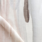 Draped fabric yardage in a watercolor paint print in shades of pink, brown and gray on a cream field.