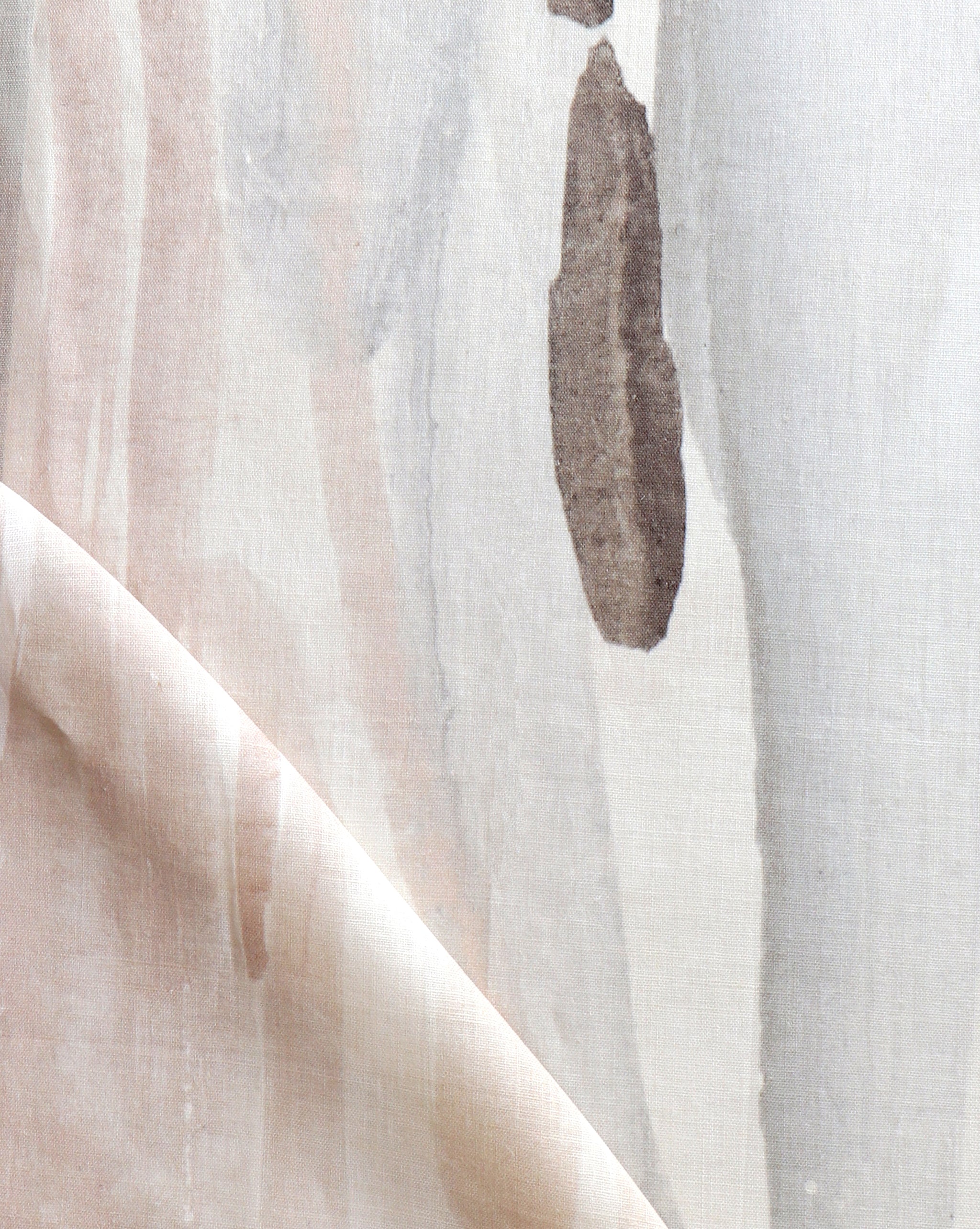 Draped fabric yardage in a watercolor paint print in shades of pink, brown and gray on a cream field.