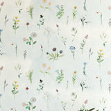 A vase of flowers stands in front of a wall covered in a painterly flower print in green and pastels on a cream field.