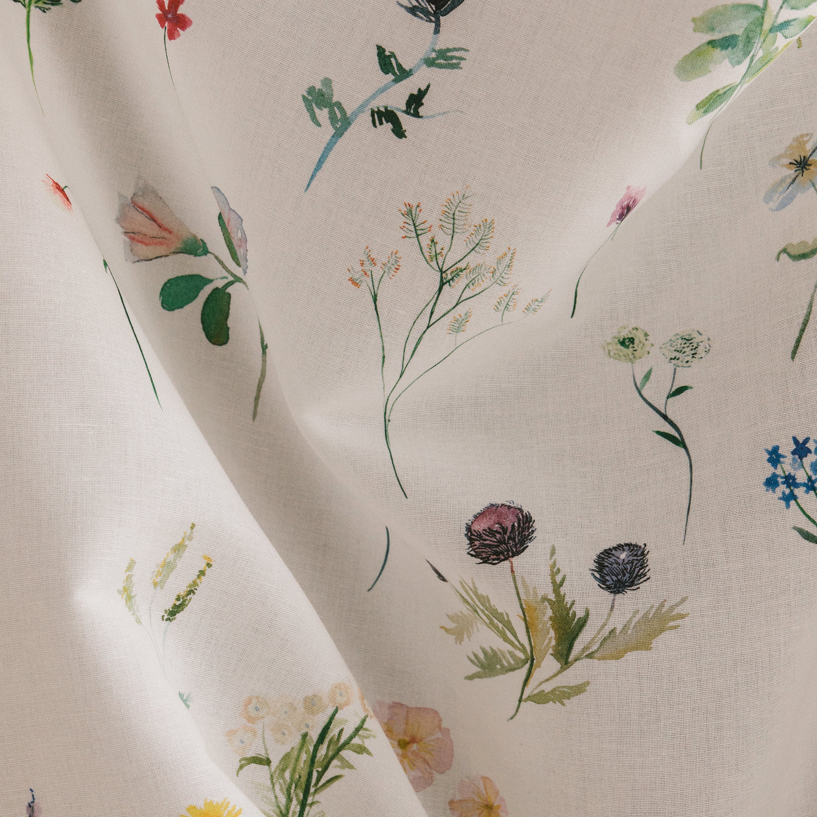 Draped fabric yardage in a painterly flower print in green and pastels on a cream field.
