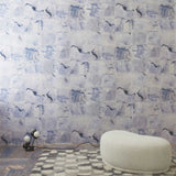 Room interior with a watercolor check wallpaper in blue featuring a white ottoman and small lamp.