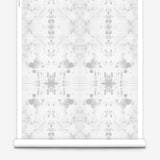 Partially unrolled wallpaper yardage in a watercolor ink blot print in gray on a white field.