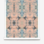 Partially unrolled wallpaper yardage in a watercolor ink blot print in blue and gray on a light pink field.