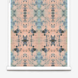 Partially unrolled wallpaper yardage in a watercolor ink blot print in blue and gray on a light pink field.