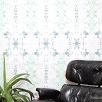 A chair and plant stand in front of a wall papered in a watercolor ink blot print in gray and green on a cream field.