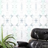 A chair and plant stand in front of a wall papered in a watercolor ink blot print in gray and green on a cream field.