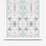Partially unrolled wallpaper yardage in a watercolor ink blot print in gray and green on a cream field.