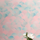 A vase of flowers stands in front of a wall papered in a repeating scalloped print in shades of blue and pink.