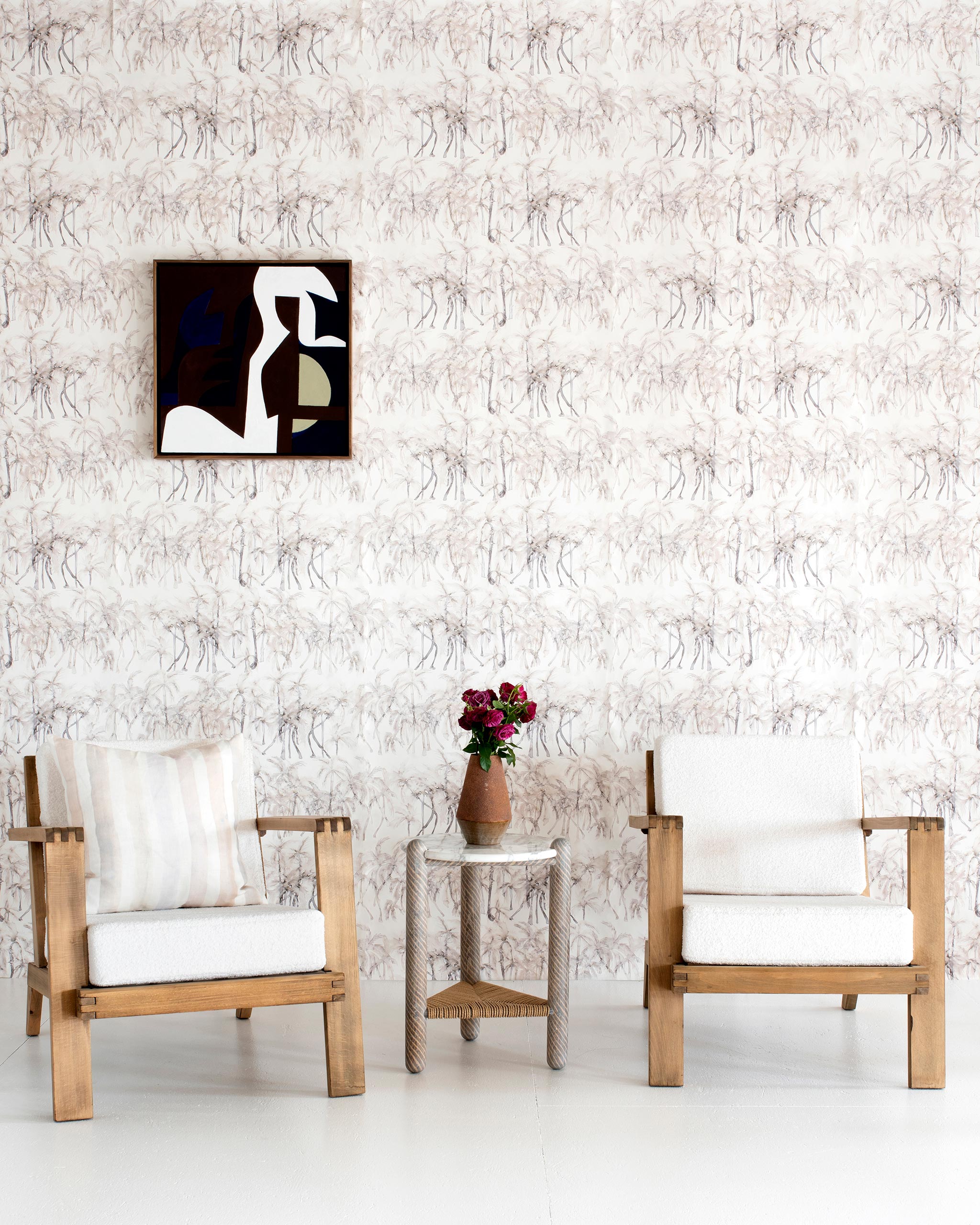 A modernist living tableau with a wall papered in a painterly palm tree stripe print in cream, gray and white.