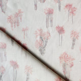 Draped fabric yardage in a painterly palm tree print in shades of pink and gray on a white field.