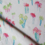 Draped fabric yardage in a painterly palm tree print in shades of pink, green and turquoise on a white field.