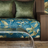 Bed with green pillows and blue floral bedspread next to a clear acrylic bench on a stone floor.