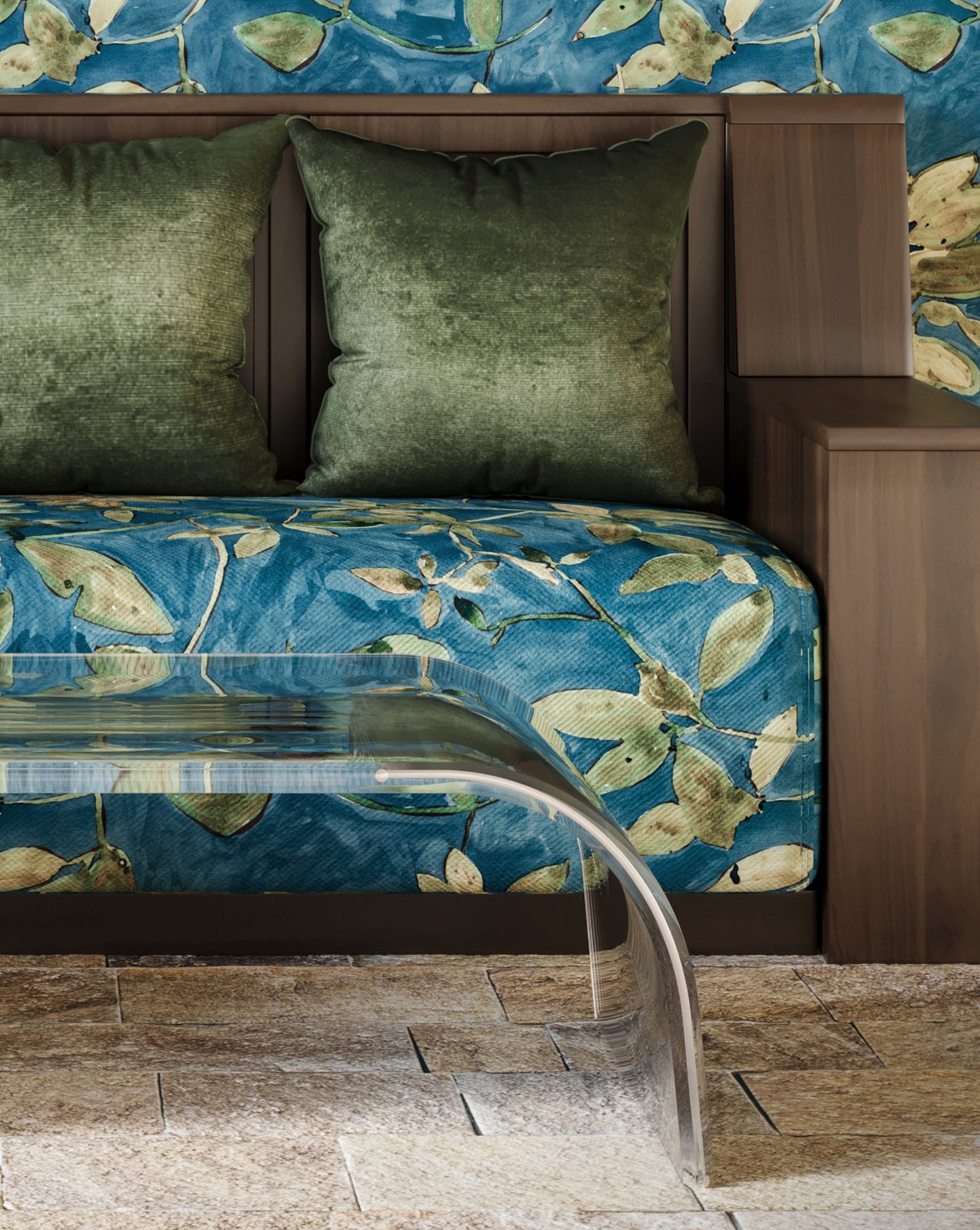Bed with green pillows and blue floral bedspread next to a clear acrylic bench on a stone floor.