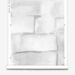Partially unrolled wallpaper yardage in a watercolor grid print in shades of gray and white.