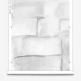 Partially unrolled wallpaper yardage in a watercolor grid print in shades of gray and white.