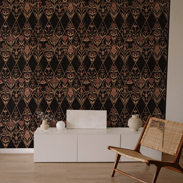 An armchair and credenza stand in front of a wall papered in a floral and diamond lattice print in pink, tan and black.