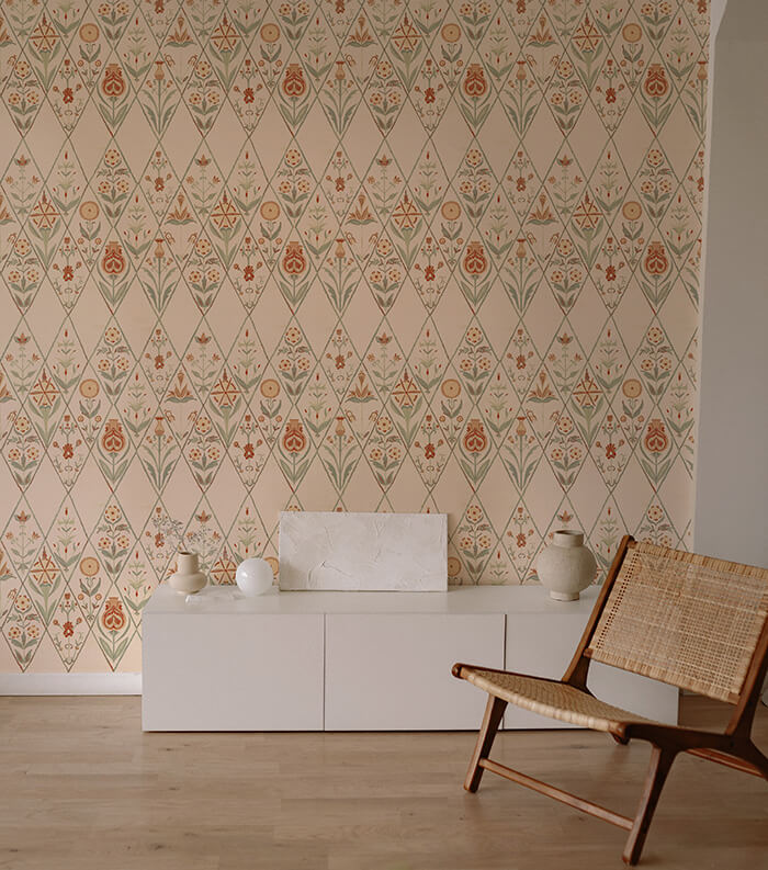 An armchair and credenza stand in front of a wall papered in a floral and diamond lattice print in green, orange and cream.