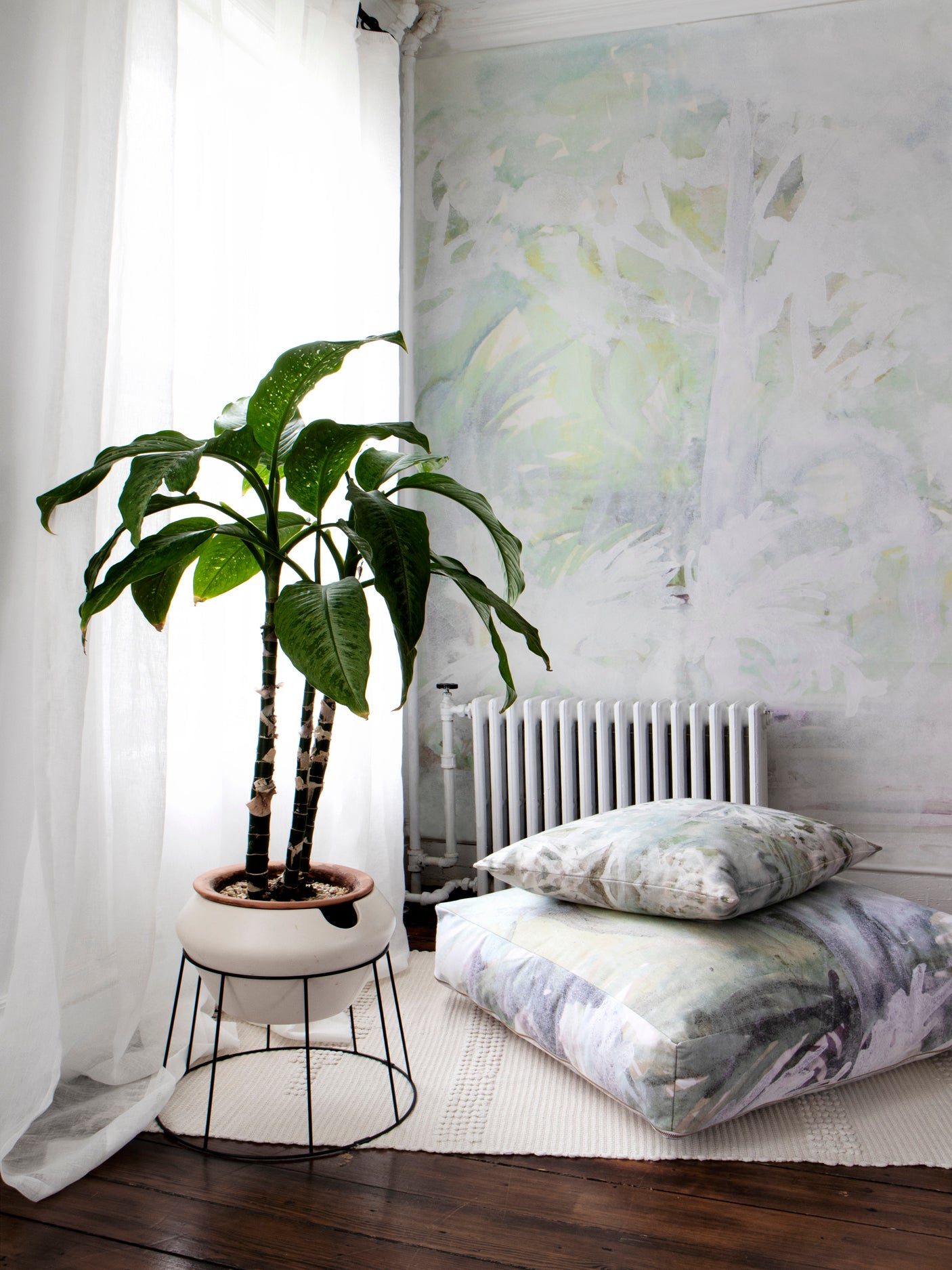 Room interior with a plant on a small table, radiator, and patterned cushions.