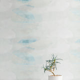 A potted plant stands in front of a wall covered in an abstract color blot print in shades of white, gray and turquoise.