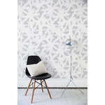 Chair and floor lamp in front of a wall papered in a bold white brushtroke pattern on a light gray background.