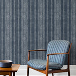 An armchair and coffee table in front of a wall papered in a striped pattern of intricate white lines over a washed denim background.