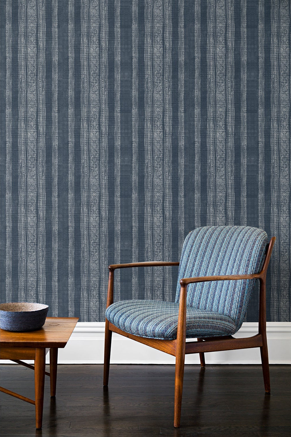 An armchair and coffee table in front of a wall papered in a striped pattern of intricate white lines over a washed denim background.