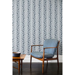 An armchair and coffee table in front of a wall papered in repeating horizontal stripes of white and charcoal branches and fruit on a light gray background.