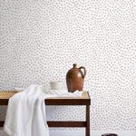 A bench with a towel and clay vases stands in front of a wall papered in a scalloped dot print in blush and white.