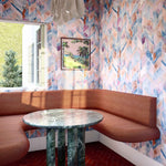 A modernist dining room with an open window and walls papered in a painterly herringbone print in blue, pink and orange.