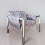 A modernist armchair upholstered in a painterly herringbone fabric in shades of blue, pink and orange.