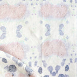 Draped fabric yardage in a watercolor inkblot print in pastel pink and purple on a cream field.