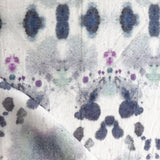 Draped fabric yardage in a watercolor inkblot print in shades of purple and gray on a cream field.