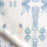Draped fabric yardage in a watercolor ink splash print in shades of pastel blue and pink on a cream field.