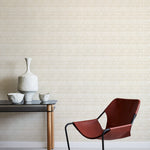 A modernist armchair stands in front of a wall papered in a playful triangular stripe print in white and light brown.