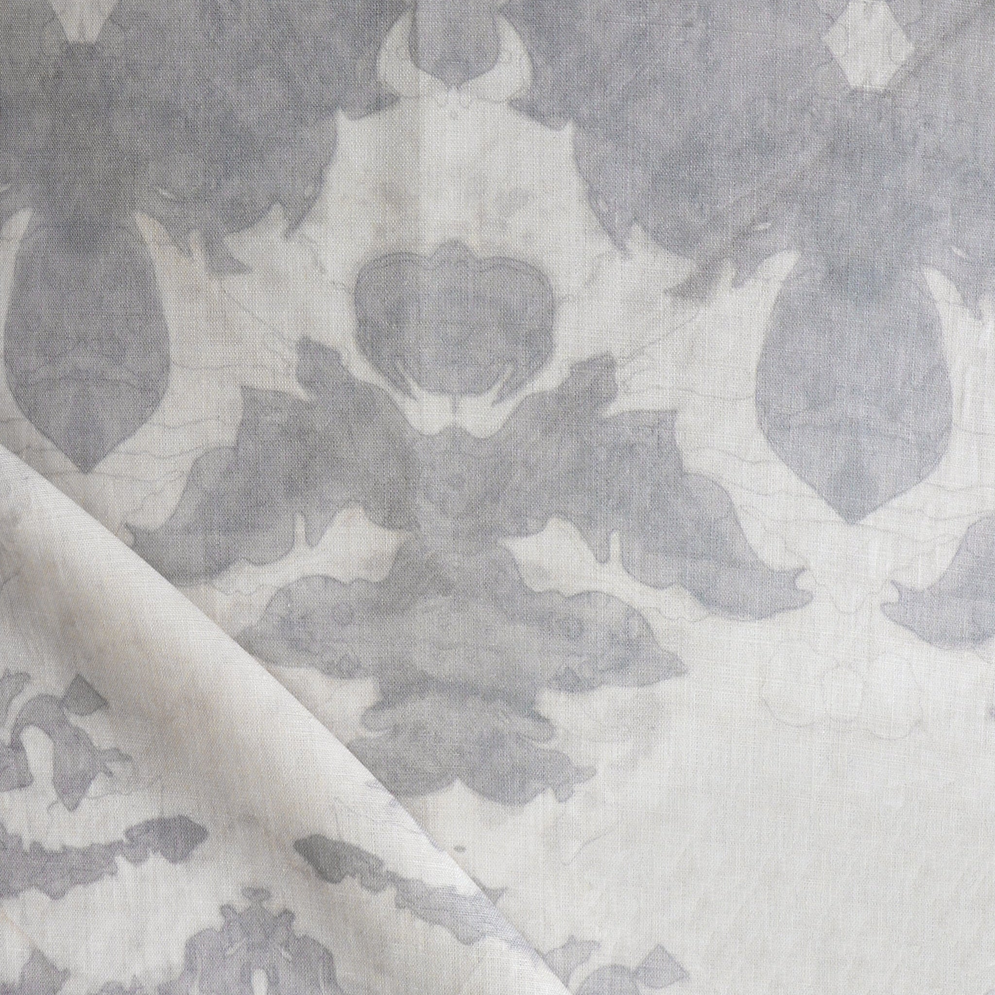 Draped fabric yardage in a watercolor ikat print in shades of gray on a greige field.