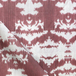 Draped fabric yardage in a watercolor ikat print in shades of red and pink on a cream field.
