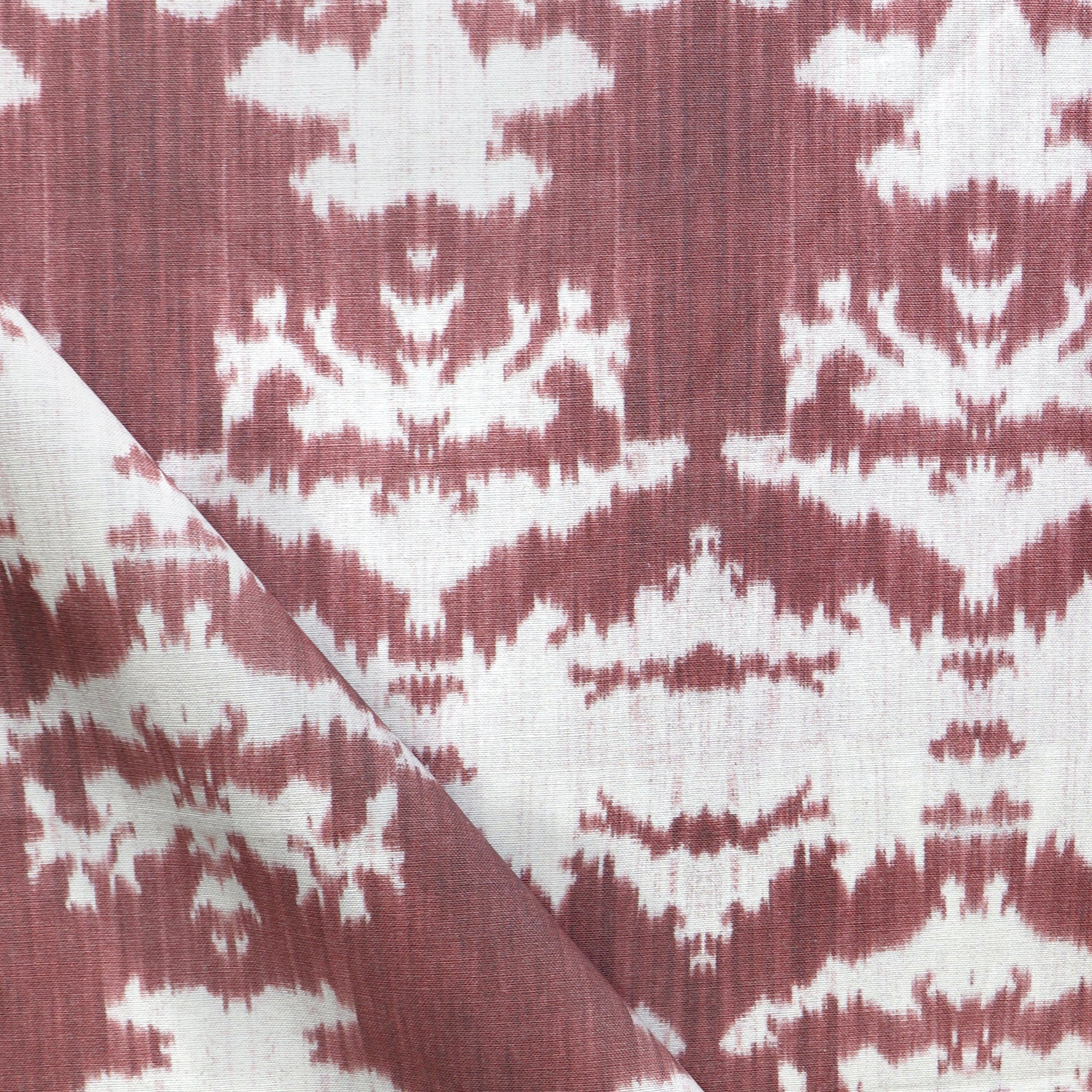 Draped fabric yardage in a watercolor ikat print in shades of red and pink on a cream field.