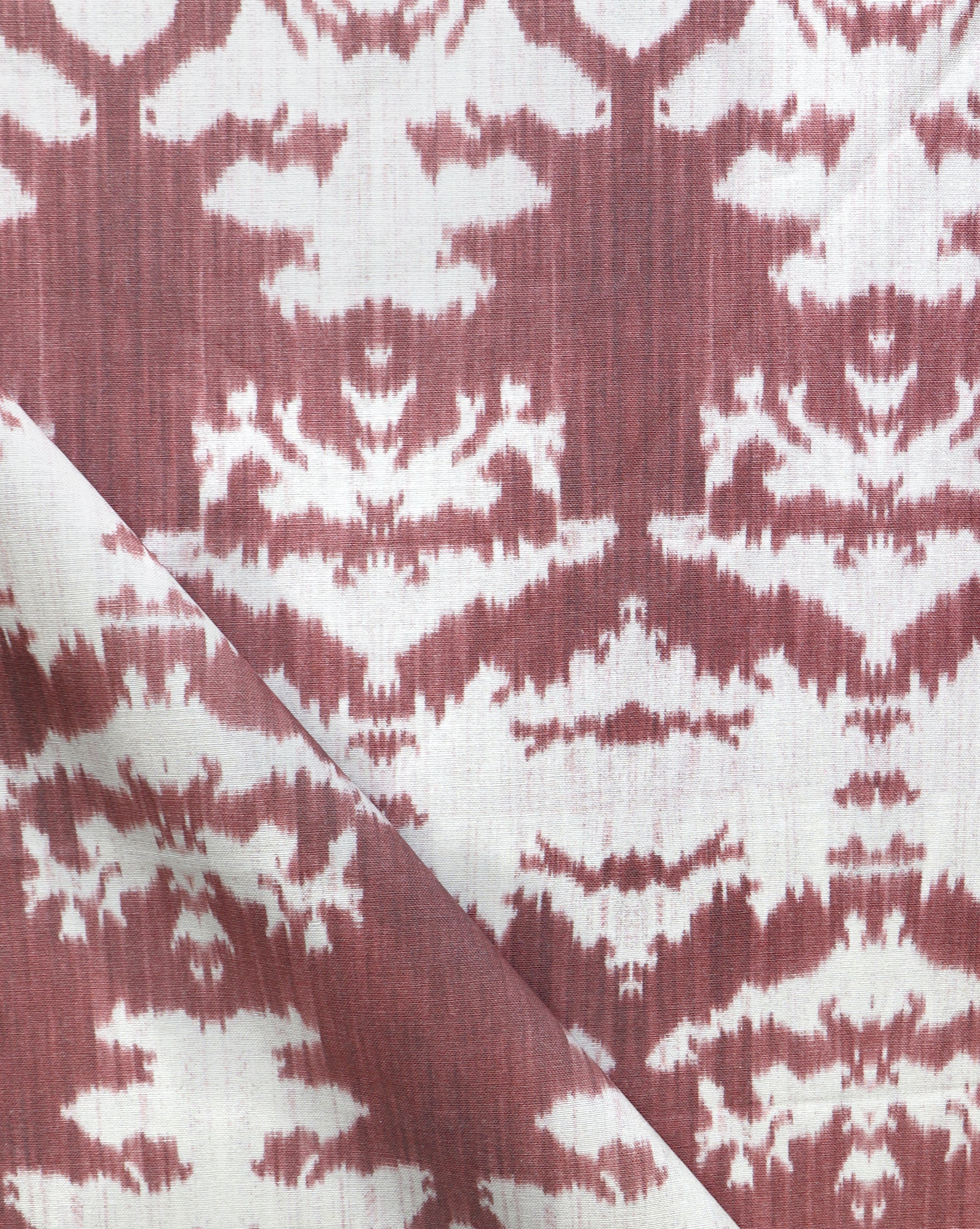 Draped fabric yardage in a watercolor ikat print in shades of red and pink on a cream field.