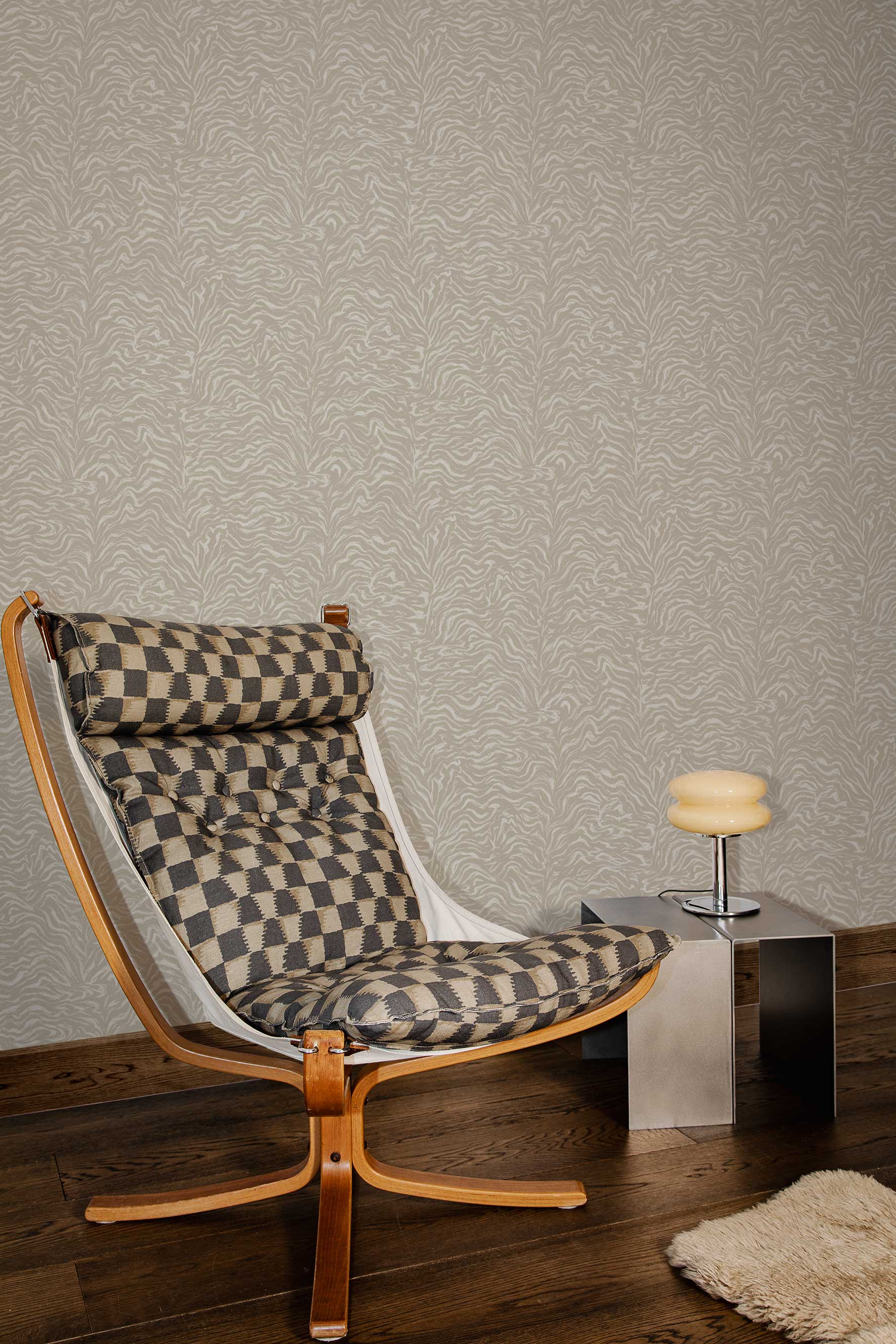 Styled interior vignette with vintage wooden butterfly style chair with tan and black cushions, steel cube side table, retro glass lamp, dark wood floor and beige zebra patterned wallpaper. 