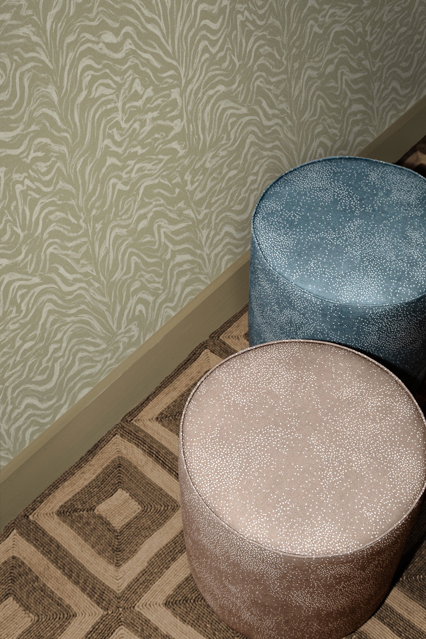 Overhead image of two upholstered cylindrical ottomans in a dotted pattern in taupe and blue against a tan zebra wallpaper and geometric brown rug.