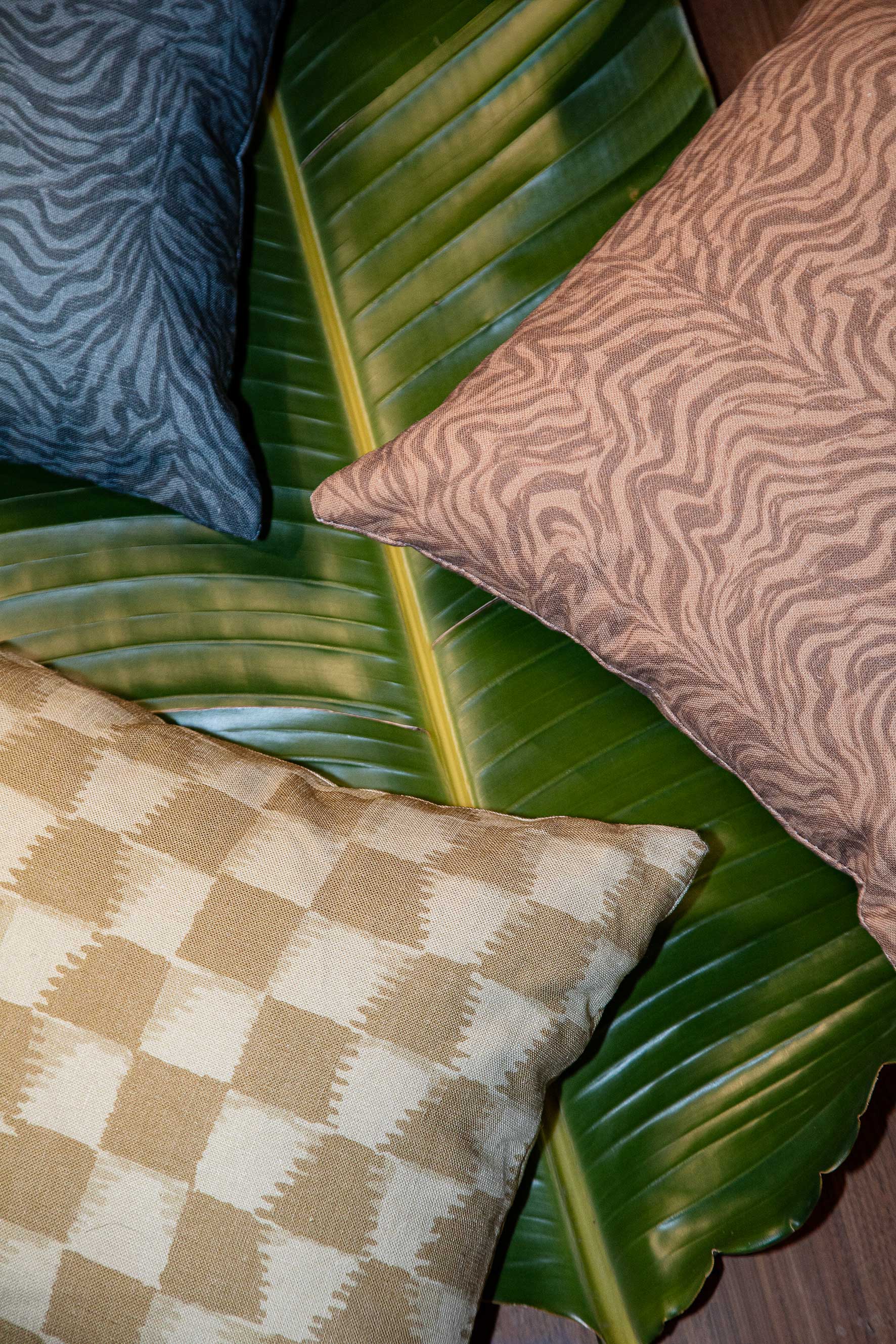 Styled flat-lay with detail of three throw pillows atop of a banana leaf with various patterns.
